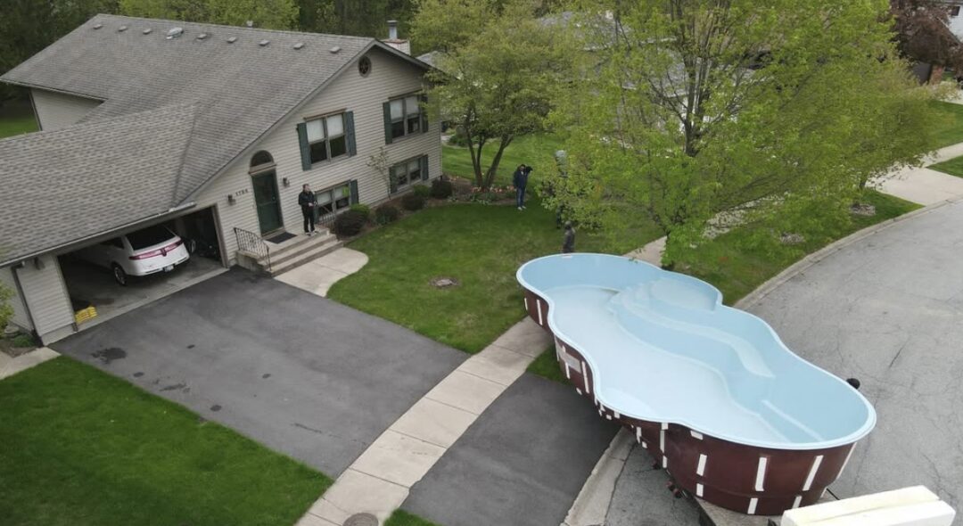 A freeform fiberglass pool being brought into a backyard.